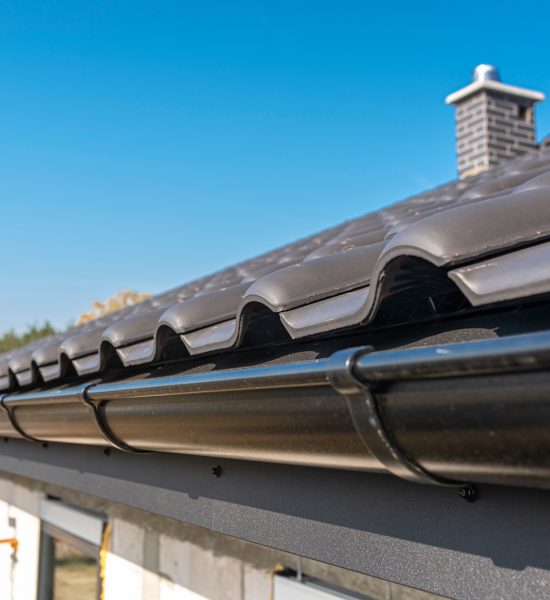 A metal, black gutter on a roof covered with ceramic tiles. Close up shot. A metal, black gutter on a roof covered with ceramic tiles. Close up shot.