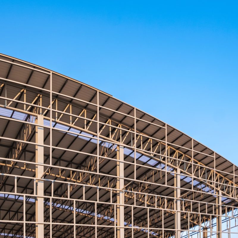 Part of large metal factory building structure in construction site against blue sky background Part of large metal factory building structure in construction site against blue sky background